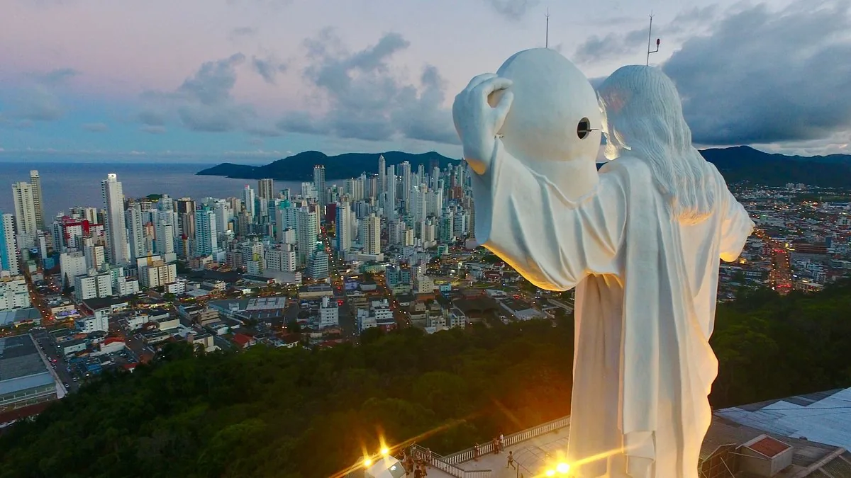 Monumento Cristo Luz iluminado al anochecer, con el skyline de Balneário Camboriú de fondo.