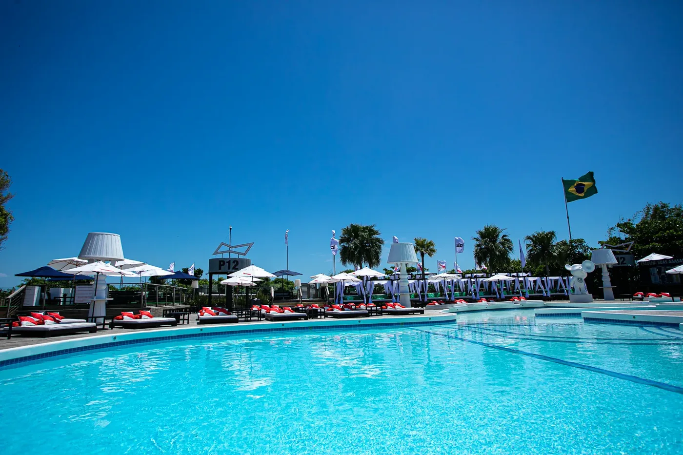 Zona de la piscina del beach club P12 en Jurerê Internacional, Florianópolis, con reposeras y día soleado.