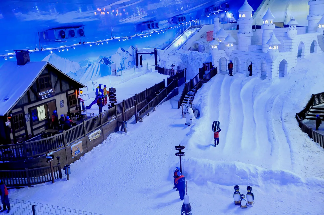 Interior del Snowland en Gramado, con nieve de verdad, castillo de hielo y gente jugando en la pista.
